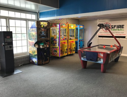 A game room featuring arcade machines, claw machines, and an air hockey table in a well-lit space.