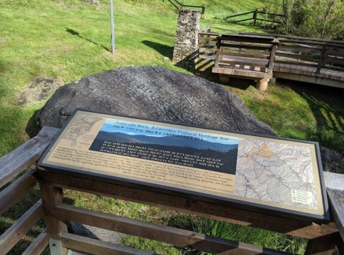 A sign at a cultural heritage site, detailing information about the area, with a rocky landscape in the background.