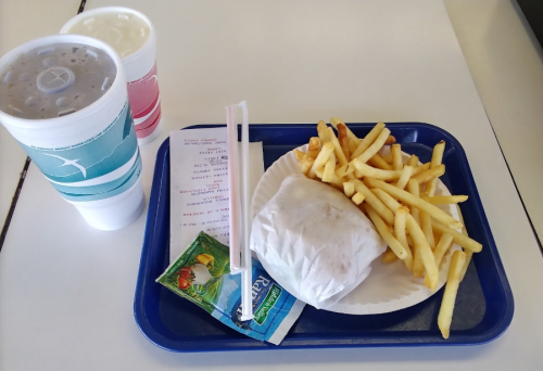 A tray with a wrapped burger, fries, a packet of sauce, and two large drinks. A receipt is also visible.