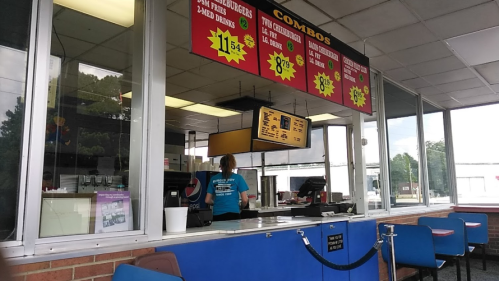 A fast-food counter with a menu display and a staff member taking orders. Brightly colored signs advertise combo deals.