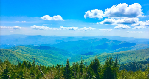 A panoramic view of lush green mountains under a bright blue sky with fluffy white clouds.