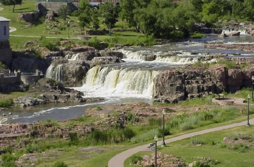 A scenic view of a waterfall cascading over rocky terrain, surrounded by greenery and walking paths.