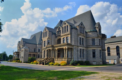 Historic stone building with intricate architecture, surrounded by greenery and under a partly cloudy sky.