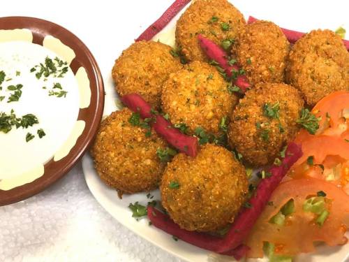 A plate of golden-brown fritters garnished with herbs, served with sliced tomatoes and a bowl of dipping sauce.