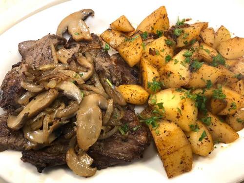 A plate featuring grilled steak topped with sautéed mushrooms and onions, alongside seasoned roasted potatoes.