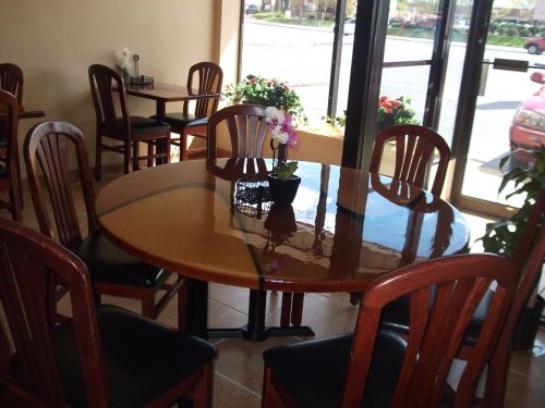 A wooden dining table with six chairs, featuring a small plant centerpiece, in a bright, inviting restaurant interior.