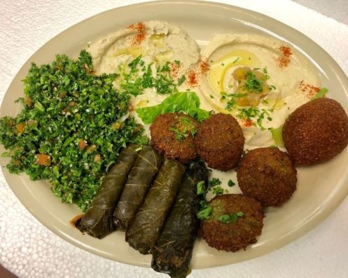 A plate featuring hummus, tabbouleh, falafel, stuffed grape leaves, and garnished with herbs.