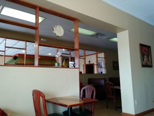 Interior of a restaurant featuring wooden tables, chairs, and a decorative wall with a flower arrangement.
