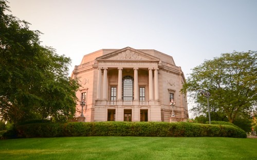 Severance Hall, a grand building with classical architecture, surrounded by lush greenery and a clear sky.
