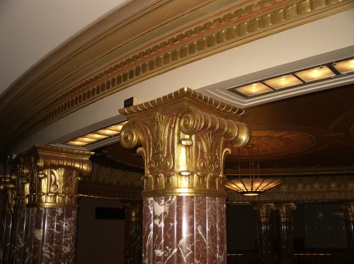Ornate golden columns with intricate designs and marble bases, set against a decorative ceiling in an elegant interior.