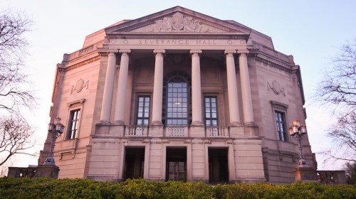 Severance Hall, a grand building with columns and large windows, surrounded by greenery at dusk.