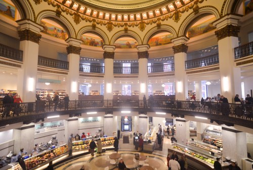 A spacious, elegantly designed interior of a market with high ceilings, arches, and bustling shoppers.