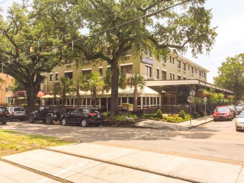 A charming restaurant with outdoor seating, surrounded by trees and parked cars on a sunny day.