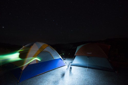 Two tents illuminated by a flashlight under a starry night sky, with a hint of green light in the foreground.