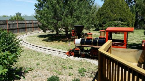 A small model train on a winding track in a grassy area, surrounded by trees and a wooden deck.