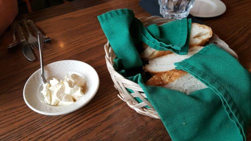 A basket of sliced bread with green napkins, next to a small bowl of cream cheese on a wooden table.