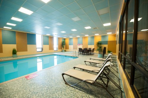 Indoor swimming pool area with lounge chairs, plants, and a dining table, featuring blue and tan walls.