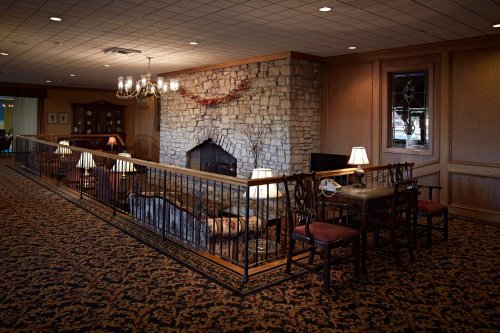 Cozy lounge area with a stone fireplace, wooden furniture, and warm lighting, featuring a patterned carpet.