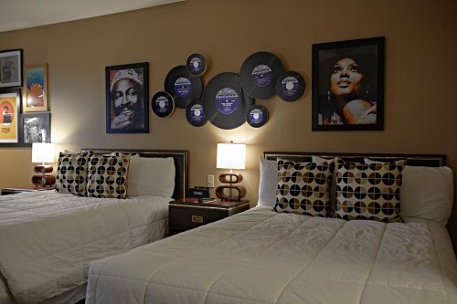 A cozy hotel room with two beds, decorative pillows, and framed art, including vinyl records on the wall.