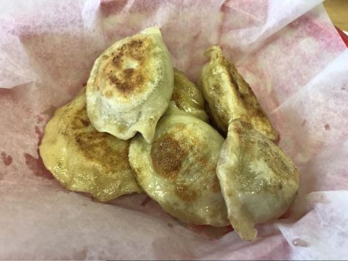 A basket lined with paper containing several golden-brown, pan-fried dumplings.