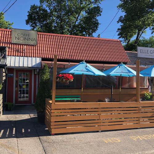 Exterior of Caffè Nonna with a red roof, outdoor seating under blue umbrellas, and a wooden fence.