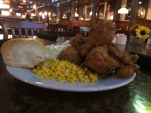 A plate of fried chicken, corn, mashed potatoes, and a biscuit, set on a wooden table in a cozy restaurant.