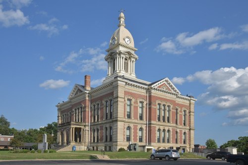 Historic brick courthouse with a clock tower, set against a blue sky with fluffy clouds.