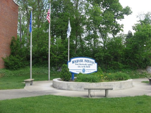 Sign for Wabash, Indiana, the first electrically lighted city in the world, surrounded by greenery and flags.
