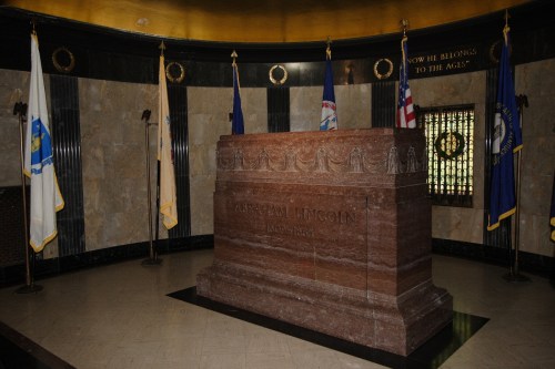 The tomb of Abraham Lincoln, surrounded by flags, in a solemn, marble-finished chamber.