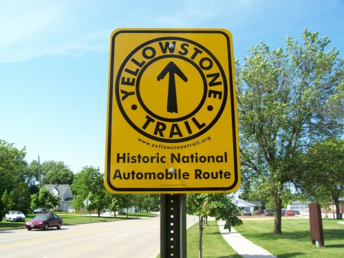 Yellowstone Trail sign indicating a historic national automobile route, set against a clear blue sky and green trees.