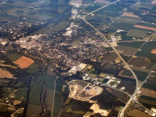 Aerial view of a small town surrounded by fields, roads, and a river, showcasing a mix of urban and rural landscapes.
