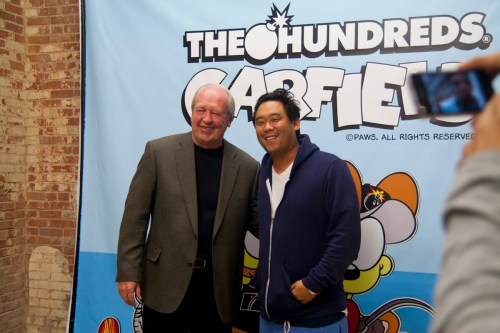 Two men pose for a photo in front of a colorful backdrop featuring cartoon characters.