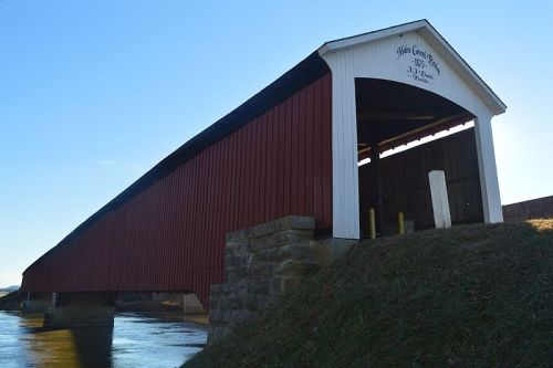 A red and white covered bridge spans a river, with a clear blue sky in the background.