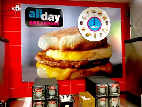 A colorful wall display featuring an all-day breakfast sandwich with a menu graphic above it.