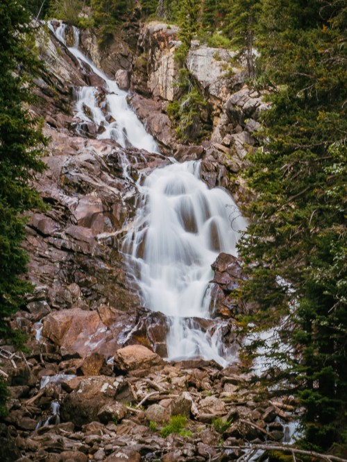 A cascading waterfall flows over rocky terrain, surrounded by lush green trees.