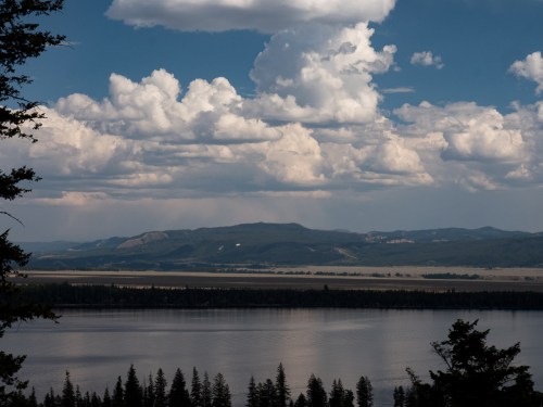 A serene landscape featuring a calm lake, distant mountains, and a sky filled with fluffy clouds.