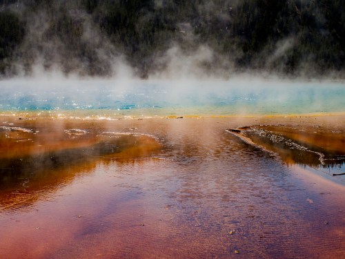 A vibrant hot spring with blue water and steam, surrounded by colorful mineral deposits and a misty landscape.