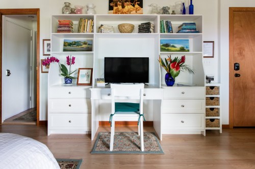 A bright room featuring a white desk with a TV, bookshelves, plants, and decorative items, creating a cozy workspace.