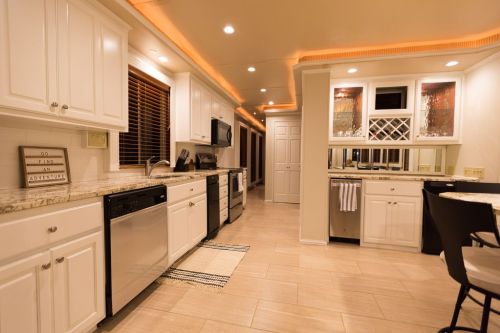 Modern kitchen with white cabinets, stainless steel appliances, and warm lighting, featuring a dining area and a hallway.