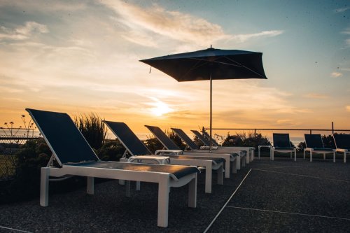 Lounge chairs under an umbrella at sunset, with a serene view of the horizon and soft clouds in the sky.