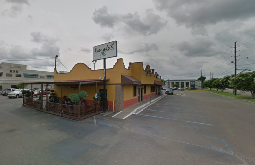 A colorful restaurant named "Avocados" with outdoor seating, set against a cloudy sky and nearby parking lot.