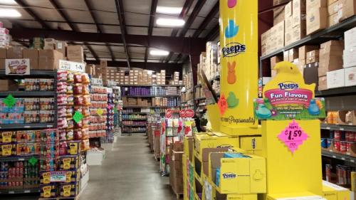 A colorful warehouse aisle filled with shelves of snacks and candy, featuring a display of Peeps Fun Flavors.