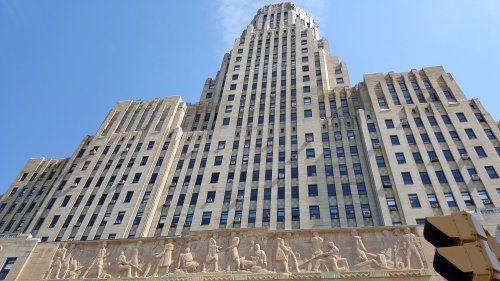 Art Deco skyscraper with intricate carvings at the base, set against a clear blue sky.