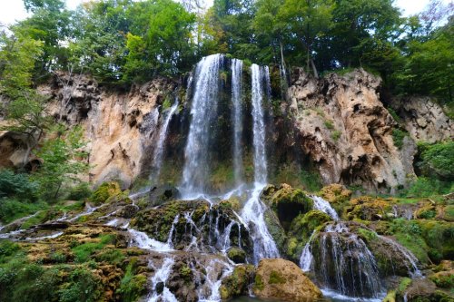 A stunning waterfall cascading down rocky cliffs, surrounded by lush greenery and moss-covered stones.