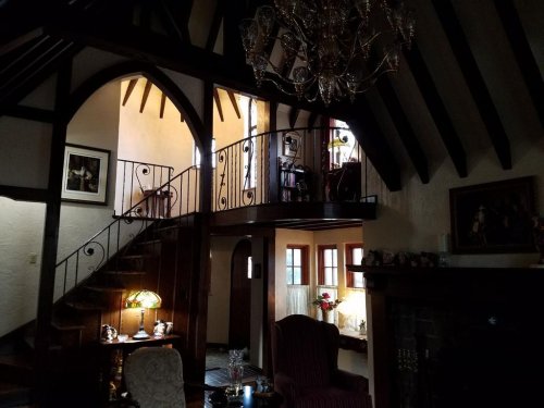A cozy interior of a home featuring a staircase, chandelier, and warm lighting, with wooden beams and elegant decor.