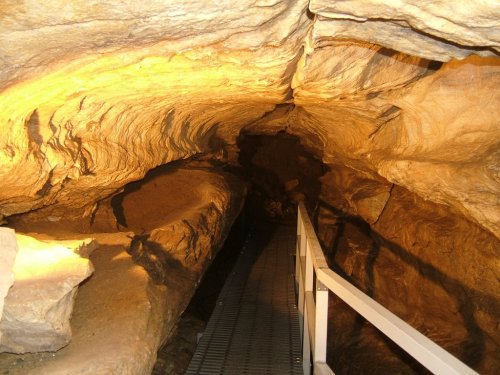 A dimly lit cave interior with textured rock formations and a metal walkway leading into the darkness.