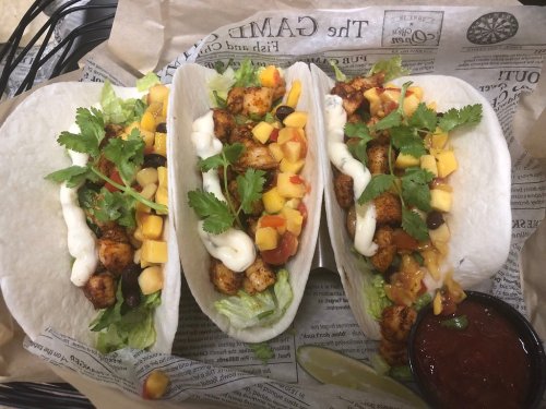 Three tacos filled with seasoned chicken, mango, black beans, lettuce, and topped with cilantro and sauce, served with salsa.