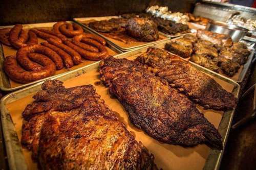 A variety of smoked meats, including ribs and sausages, arranged on trays with a smoky background.