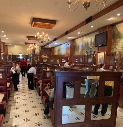 A bustling diner interior with wooden booths, chandeliers, and patrons enjoying their meals.