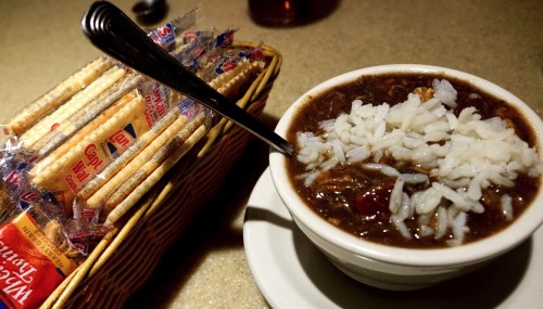 A bowl of stew topped with rice, next to a basket of crackers on a table.